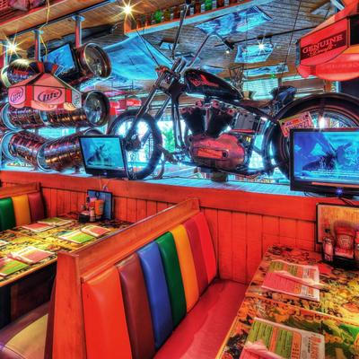 Diner interior, rainbow-colored booths, Above, a motorcycle and TV screens hang