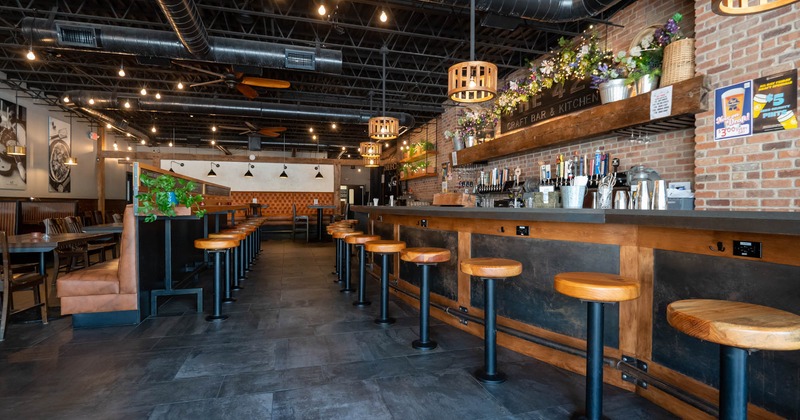 Interior of a modern bar with a long wooden counter and stools, brick walls, hanging lights