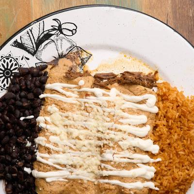 Enchiladas, topped with tomatillo sauce, sour cream, and cheese, with rice, and beans.