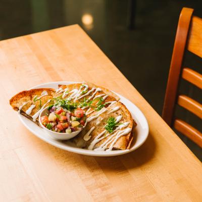 Quesadilla topped with sauce and a small bowl of fresh salsa.
