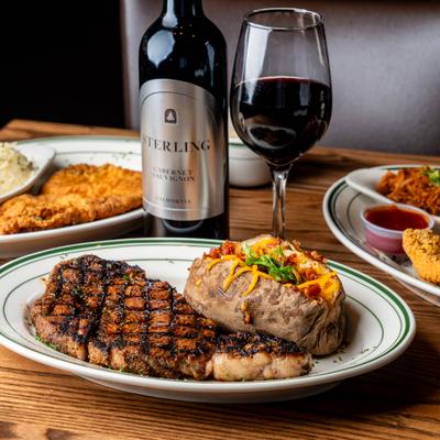 Grilled ribeye steak accompanied by a loaded baked potato and paired with red wine.