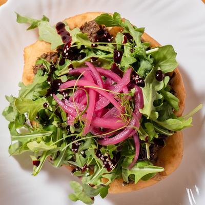 Elk birria frybread topped with arugula and pickled red onions.