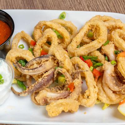 Fried calamari, served on a white plate with cups of tzatziki and marinara.