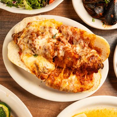 Meatball Parmigiana sandwich on a plate, surrounded by assorted dishes.