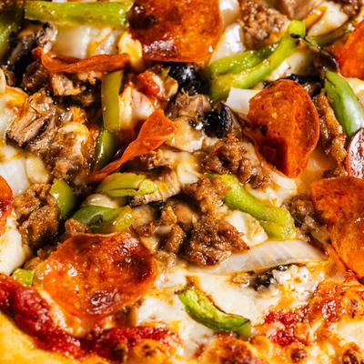 Close-up of a supreme pizza loaded with pepperoni, sausage, onions, green peppers, and mushrooms.