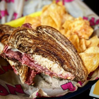 A Reuben sandwich served with a side of potato chips.