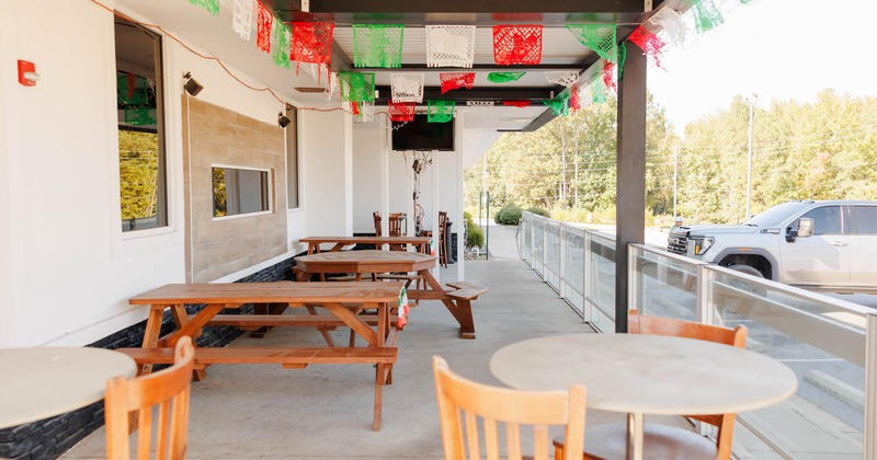 Outdoor seating area with wooden tables, colorful banners, and a parking lot view