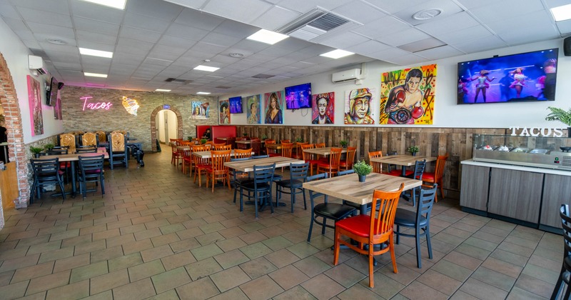 Colorful interior with wooden tables, chairs, vibrant paintings and neon "Tacos" sign