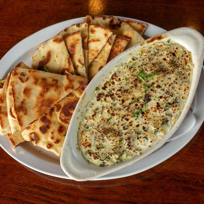 Spinach and artichoke dip served with naan on a white plate, top down view.