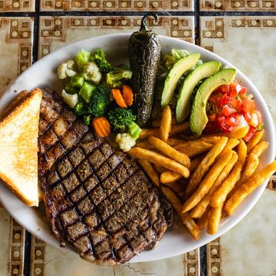 Ten ounce rib eye steak with fries, vegetables and toast.