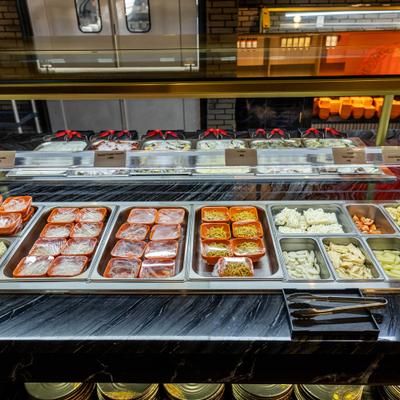 Refrigerated buffet bar featuring pre portioned meat cuts and various side ingredients.
