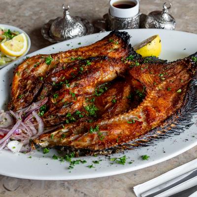 Grilled fish topped with herbs, served with sliced onion and a lemon wedge.