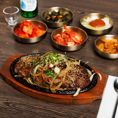 Bassack Bulgogi served on a cast-iron skillet, alongside traditional side dishes.