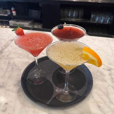 Three colorful cocktails with fruit garnishes on a tray.