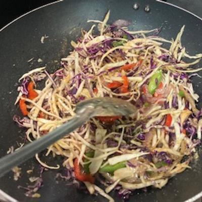 A stir-fry with cabbage and green and red bell peppers in a pan