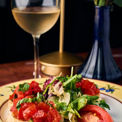 Bruschetta topped with tomatoes and greens on a  plate beside a wine glass.