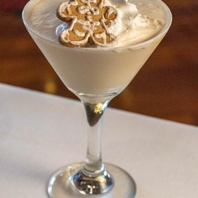 A creamy cocktail in a martini glass topped with whipped cream and a gingerbread cookie.