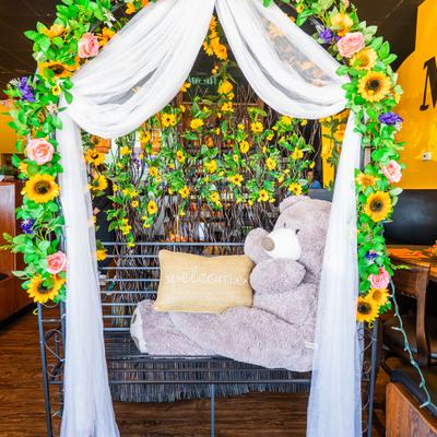 Decorative setup with iron bench with a sunflower and rose archway and a large teddy bear.