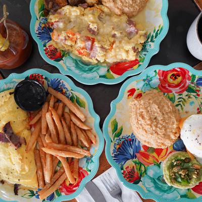 Three colorful plates featuring two omelets, fries, grits, and an avocado biscuit.