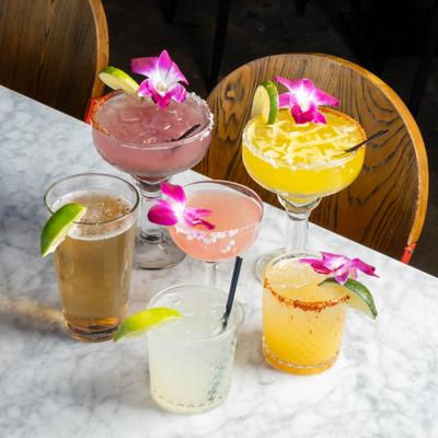 Assorted cocktail drinks and a glass of beer on a white marble countertop.