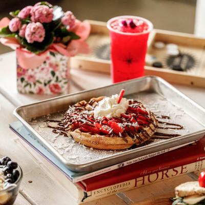 Waffle served on a tray, alongside floral arrangement and a iced drink.