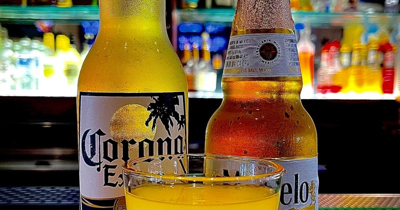 A layered yellow and red cocktail rests on a bar counter with two bottles of beer