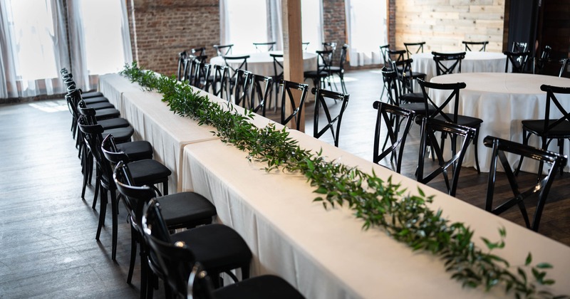 Long dining tables with white tablecloths and green foliage centerpiece