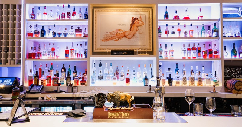 A modern bar with shelves of illuminated bottles and elegant decor