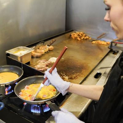 A kitchen staff member flipping an omelet in a frying pan on a busy grill.