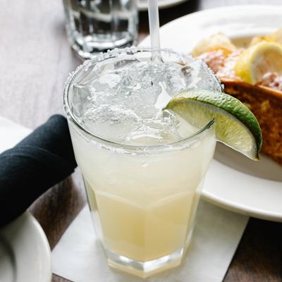 A margarita with a salted rim and lime wedge sits on a table with a food plate.
