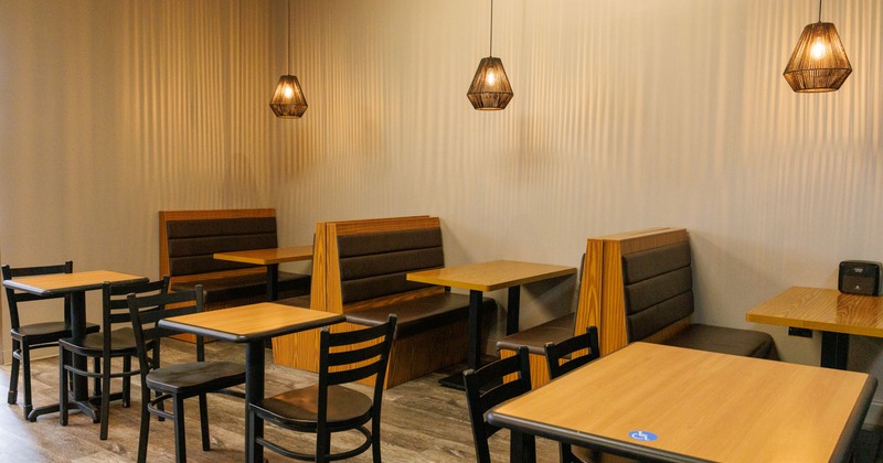 Modern interior with wooden tables, chairs, booth seating and pendant lighting.