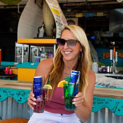 A customer sitting on a bar stool, holding drinks and smiling.