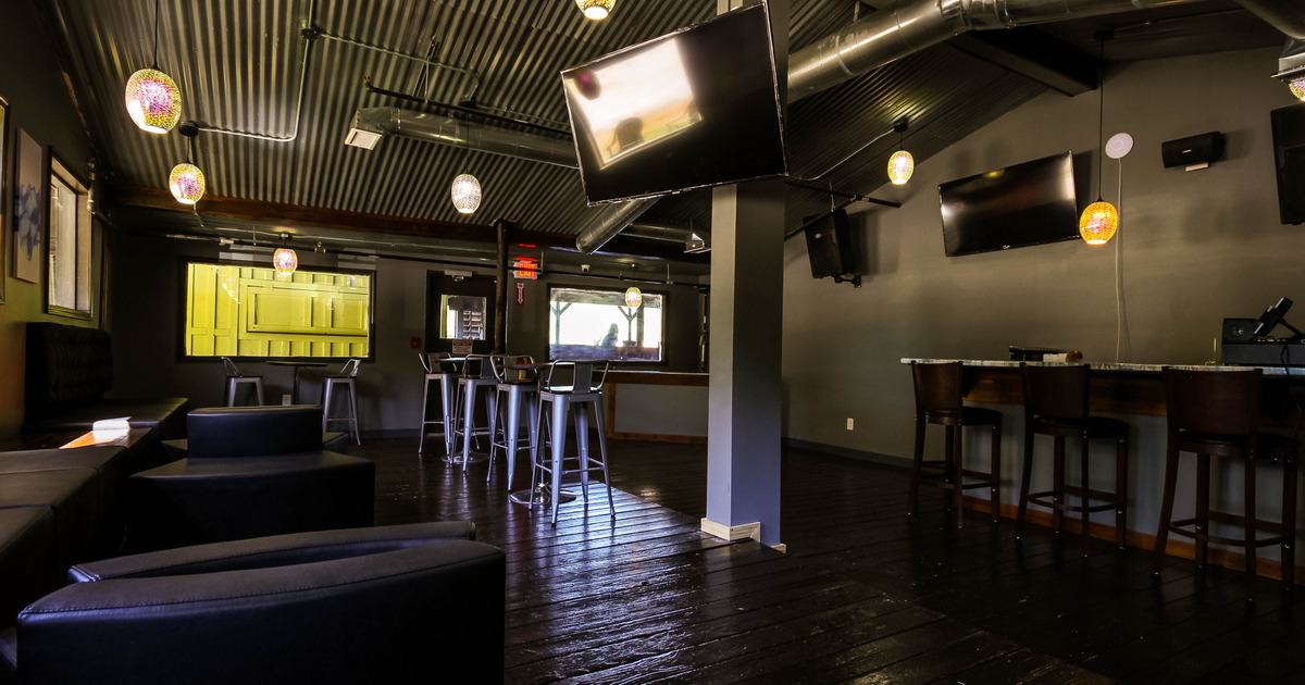Restaurant interior, tables and booths on the left, flat screens attached to the wall and a couple of windows in the back