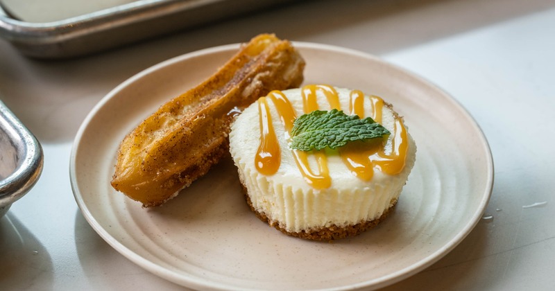 A mini cheesecake with caramel syrup served next to a churro