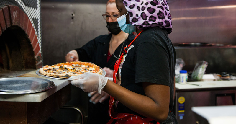 Kitchen staff taking a freshly baked pizza out of the oven