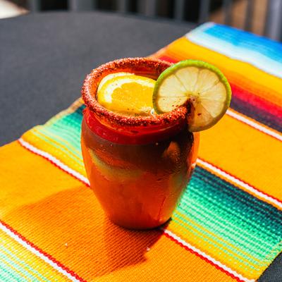 Cantarito cocktail in a clay mug garnished with orange and lime slices.