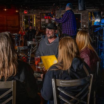 A group of customers is enjoying drinks at a table while a musician is performing on the stage.