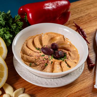 Bow of red pepper hummus topped with olives and herbs.