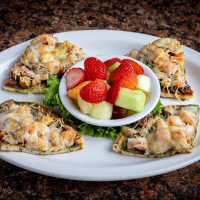 Four slices of a Chicken Pesto Flatbread and a small bowl of fruit.