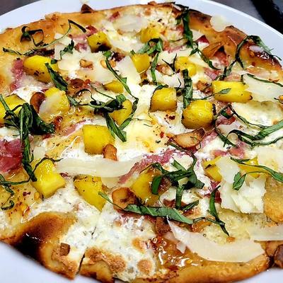 Pizza with pineapples, cheese, onion, parsley, olive oil, and prosciutto