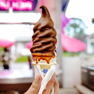 A hand holding a chocolate-dipped soft serve ice cream cone.