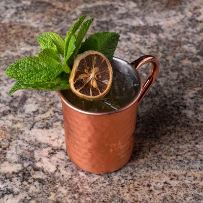 Moma Melon Fizz cocktail served in a copper mug with dry citrus and mint leaves.