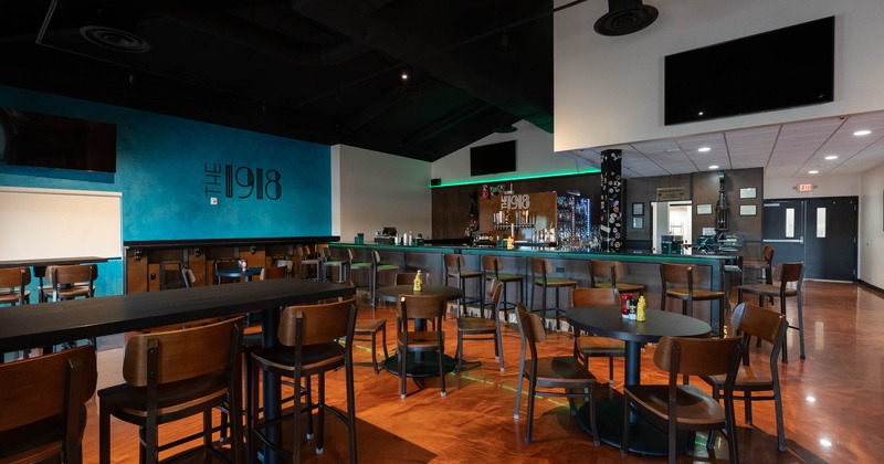 Interior, tables and chairs, high seating table with bar stools, bar, restaurant logo on the wall