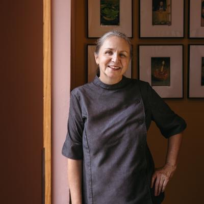 Chef in a gray uniform smiling indoors near a gallery wall.