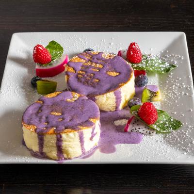 Souffle pancakes topped with purple sauce and garnished with fresh fruit.