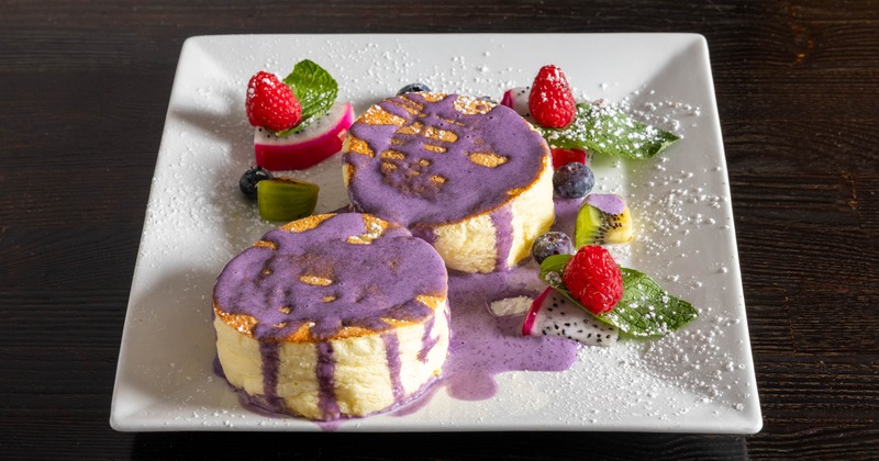 Two souffle pancakes with purple sauce and fruit