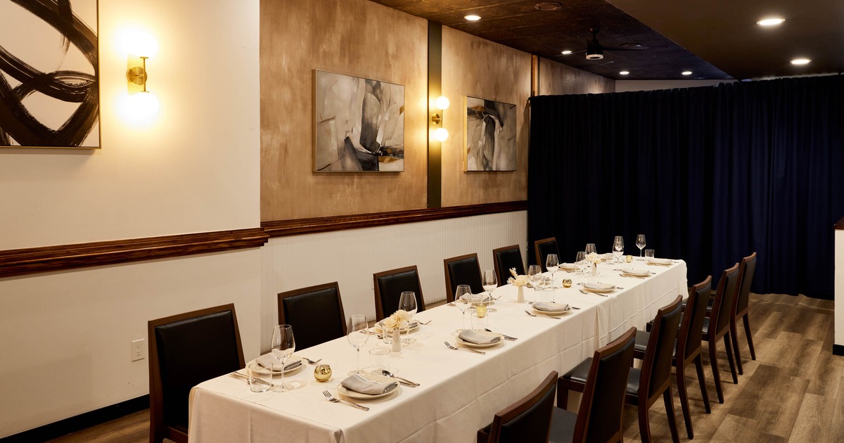 An elegant dining room with a long table set for sixteen, featuring modern art and warm lighting