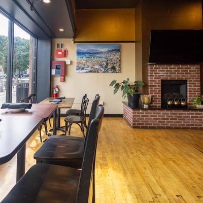 Restaurant interior with high-top seating, brick fireplace, and large windows.