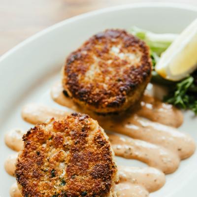 Pan-seared crab cakes served with a sauce and a lemon wedge.