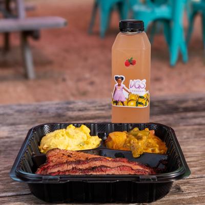Takeout container with smoked brisket, potato salad, stewed veggies, and a bottle of lemonade.